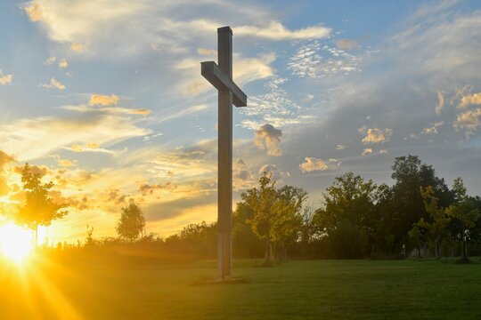 A large Christian cross in the landscape. A Christian cross illuminated by the sunset or sunrise. The concept of Christianity, spirituality, and enlightenment. - Powered by Adobe