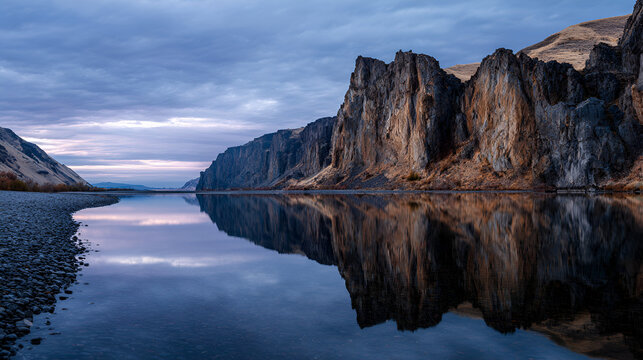 Calm lake reflecting towering cliffs under a cloudy sky at dusk creating a serene atmosphere - Powered by Adobe