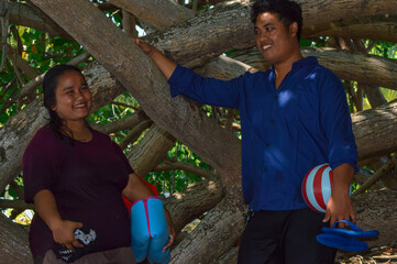 The couple pauses under the shade of seaside trees, holding supplies and sharing a quiet moment...