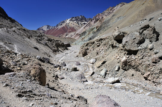 A sandy desert between gray mountains with snow on top. A river bed between the mountains. A view of desertification in a mountainous area