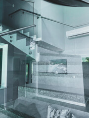 A sleek interior space features a modern staircase built from polished stone steps with glass railings and metal accents.