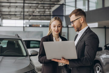 Portrait of two workers with laptop inside car showroom