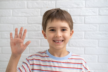 Emotional portrait of caucasian smiling little boy wearing striped t-shirt, stretching his right hand up for greeting. Happy child waving hand, say Hi