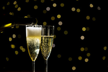 Hand pouring sparkling bubbling champagne into a glass on a festive background, close up shot. Happy New Year and Happy Birthday concepts.