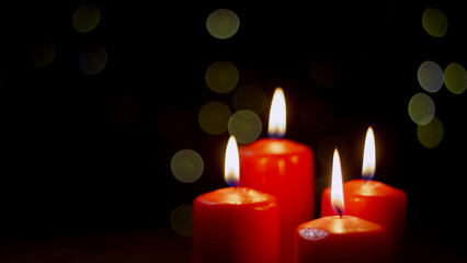 Four burning red candles on a festive black background with golden decoration, close-up shot. Advent, Christmas, holiday, and tradition concepts.
