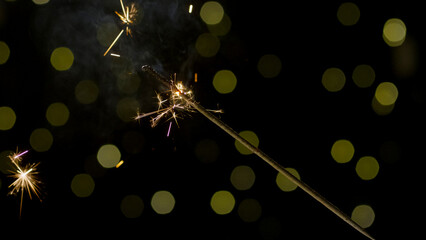 Sprinkler burning on a black background with festive golden lights, close up shot. Happy New Year concept.