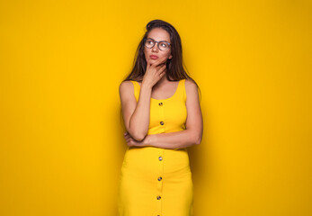 Obraz premium Decisions. Young woman thinking. Portrait of thoughtfully girl with confusion face expression, isolated on yellow background.