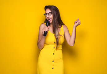 Funny woman singing on microphone, isolated on yellow background. Happy female singer.