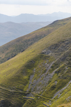 View of rugged slopes cascade downwards with a tapestry of green and grey, the distant mountains fading into a soft blue, Isola del Gran Sasso D'italia, Abruzzo, Italy.