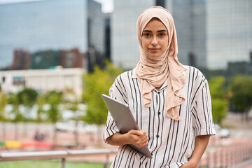 Young muslim woman student holding laptop outdoors