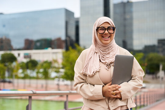 Muslim businesswoman wearing hijab and glasses smiling in city - Powered by Adobe