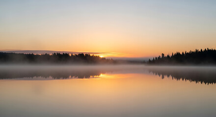 Obraz premium Misty sunrise over a calm lake with reflections of the trees and sky.