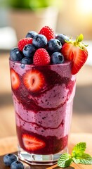 A refreshing, vibrant smoothie, topped with a mix of fresh blueberries, raspberries, and strawberries, sits in a clear glass, showcasing a beautiful layered pattern.