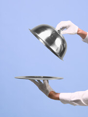 Hands lifting silver cloche from tray on blue background. Concept of unveiling gourmet dishes, presenting business products, catering service, and elegant food delivery. Negative space for ads
