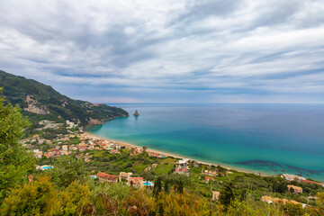 Fototapeta premium Picturesque view of the coast of the Greek island of Corfu with a beach and turquoise water under a cloudy sky, background or wallpaper for the project