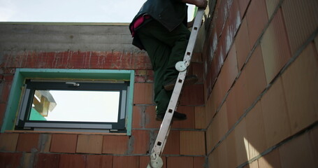 Construction workers descending ladder carefully on unfinished building site, maintaining safety...