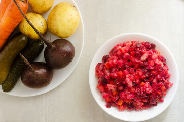 Salad vinaigrette in a white bowl with ingredients on a gray table. Vegetable salad of boiled beets, potatoes, carrots, pickles, sauerkraut and beans. Horizontal orientation. Selective focus. Top view