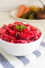 Salad vinaigrette in a white bowl on a napkin on a gray table. Vegetable salad of boiled beets, potatoes, carrots, pickles, sauerkraut and beans. Vertical orientation. Selective focus.