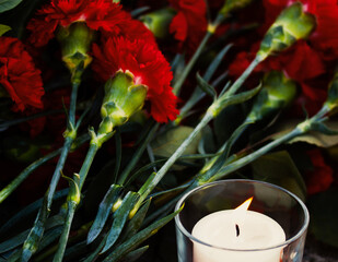 A memorial candle and red carnations. A symbol of remembrance and grief.