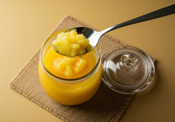 Golden Ghee Drizzles from a Wooden Spoon into a Glass Jar.