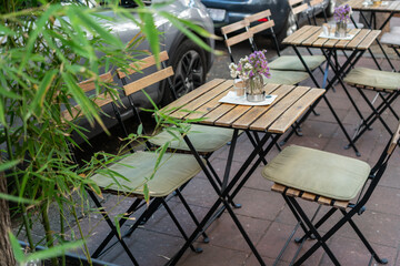 An empty street cafe or restaurant terrace with wooden tables and chairs surrounded by greenery, no people.