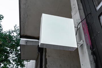 A white modern sign hangs on the wall on a city street. Copy empty space