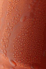 Macro photo of condensation water droplets on a textured red-orange surface. Abstract background showcasing moisture, freshness, and texture.