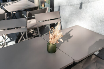 An empty street cafe or restaurant terrace with gray tables and chairs and small dried flowers composition, no people, minimalism