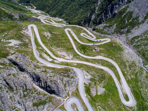 Aerial view of a dramatically winding road snaking through rugged, rocky terrain, a testament to human engineering against the stark beauty of nature, Gotthard Pass, Ticino, Switzerland.