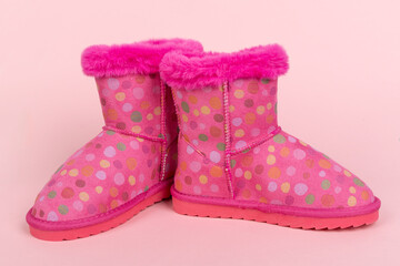 Fashionable children's winter boots. A pair of pink polka dot boots with bright faux fur, perfect for cold weather. Cute kids' footwear on a pink background.