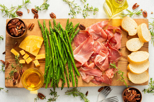 A beautifully arranged charcuterie board featuring slices of ham, blocks of cheese, fresh asparagus, and crunchy nuts. Perfect for enjoying with friends and family during special moments