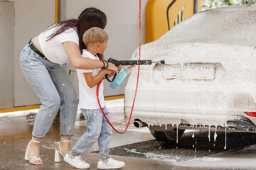 Mother and son washing car together with high pressure washer at outdoor self-service car wash on summer day, family activity and bonding time  