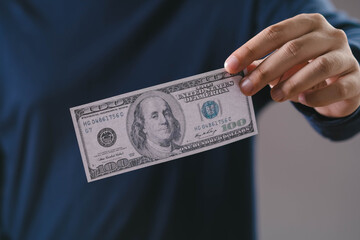 Hand holding a single US 100 dollar bill, symbolizing money, finance, cash flow, savings, payment, and currency. Perfect for articles about personal finance, investment, or economic topics.