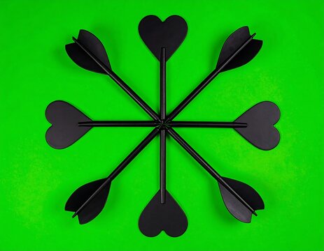 Black dart tips arranged in a circular pattern on a vibrant green background - Powered by Adobe