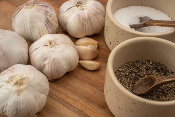 Garlic cloves and bowls of seasoning arranged on wooden surface for culinary preparation in a rustic kitchen setting