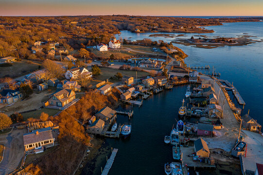 Aerial view of golden light bathing the quaint harbor village, highlighting the contrast between the rustic docks and the serene waters of Menemsha, Martha's Vineyard, Massachusetts, United States.