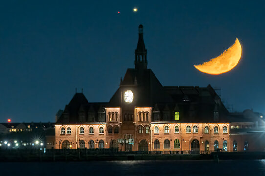 View of a crescent moon casting a golden glow over a building with illuminated windows, reflecting on the water below, Moon in New York City, New York, United States.