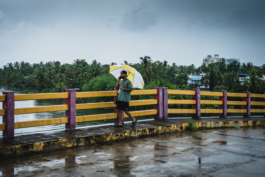 Man carrying an umbrella walking across a colorful bridge on a rainy day in Kochi, Kerala, India