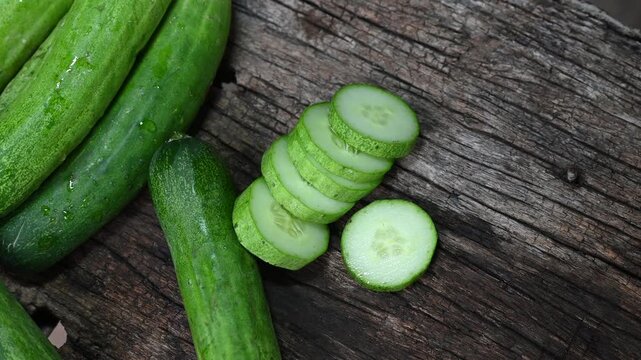 cucumber (Cucumis sativus) and slices on wood background. Freshly sliced mini cucumbers with knife on wooden cutting board.