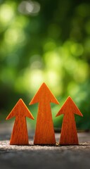 Three orange wooden upward-pointing arrows on a rustic surface, blurred green background