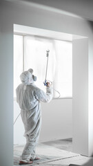 A master painter in a protective white suit paints and primes walls with a machine