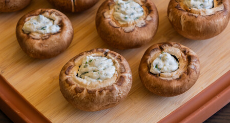 raw champignon mushrooms stuffed with herb cream cheese, arranged on a tray and ready to bake
