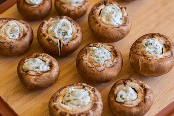 raw champignon mushrooms stuffed with herb cream cheese, arranged on a tray and ready to bake