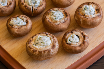 raw champignon mushrooms stuffed with herb cream cheese, arranged on a tray and ready to bake
