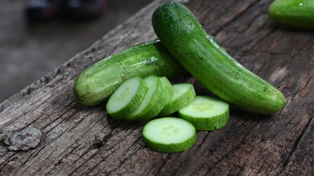 cucumber (Cucumis sativus) and slices on wood background. Freshly sliced mini cucumbers with knife on wooden cutting board.