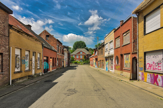 Wide shot of deserted main street showing boarded-up colorful houses under bright daylight. Low angle perspective captures urban decay and abandonment in this Belgian village of Doel.