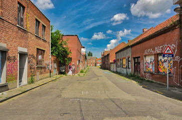 Obraz premium Wide street view of abandoned residential area with boarded brick houses covered in street art. Bright daylight captures urban decay atmosphere in depopulated settlement. In Doel Belgium.