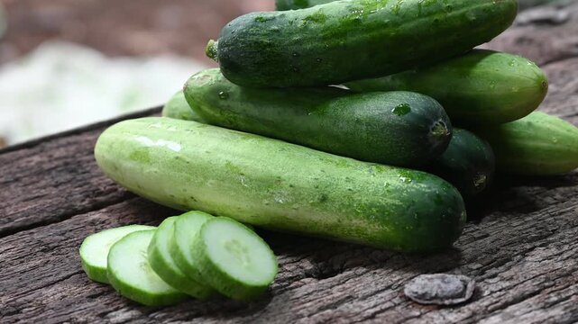 cucumber (Cucumis sativus) and slices on wood background. Freshly sliced mini cucumbers with knife on wooden cutting board.