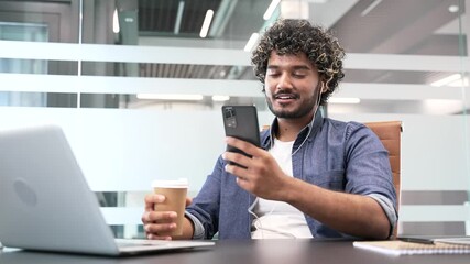 Smiling businessman is using browsing mobile phone holding a cup of coffee while sitting at workplace in a business office. Handsome worker is chatting online or reading writing message on smartphone - Powered by Adobe