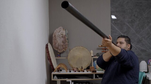 Focused man practicing circular breathing while playing a traditional didgeridoo. Ethnic music and sound therapy session in a studio